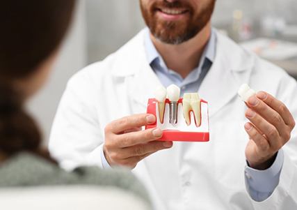 a dentist holding a model of a dental implant