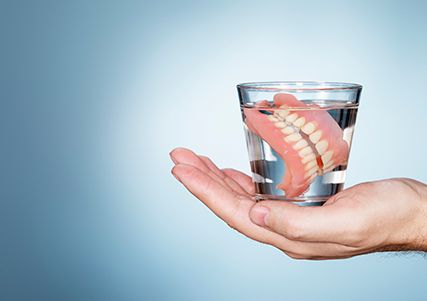 Full set of dentures in a glass of water held by a hand