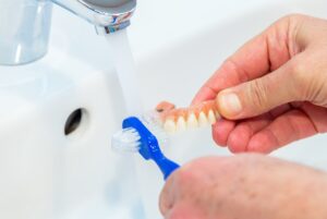 Hands brushing implant denture in a sink
